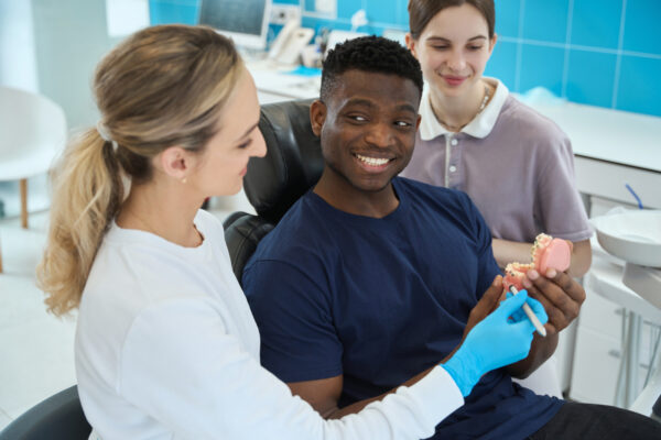 Smiling African American client satisfied with dental prosthetics way Smiling African American client satisfied with dental prosthetics way the stomatologist and nurse advising to him, aesthetic dentistry